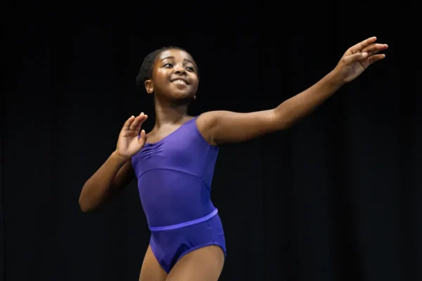 Junior dancer in a purple leotard with one arm extended on stage