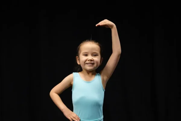 Mini dancer in turquoise SA Dance leotard posing with one arm raised