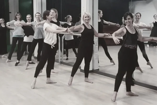 Adult dance class standing in line with arms extended during a barre exercise in the SA Dance studio